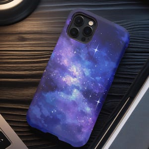 May include: A purple and blue galaxy phone case with a watercolor effect and white stars. The case has a cutout for the camera lens.
