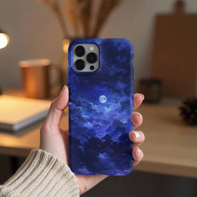 Puede incluir: Funda de tel&eacute;fono azul con un dise&ntilde;o de cielo nocturno, que presenta una luna llena y nubes. La funda tiene un acabado brillante y est&aacute; dise&ntilde;ada para un tel&eacute;fono inteligente. La funda est&aacute; sujeta en una mano.