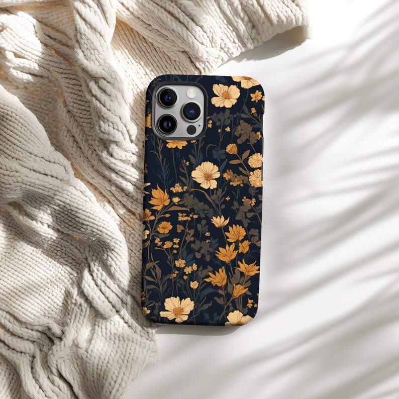 May include: A black phone case with a floral pattern featuring yellow and white flowers on a dark blue background.