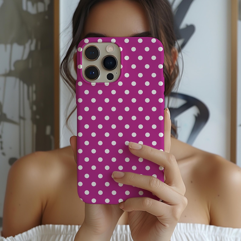 May include: A magenta phone case with a white polka dot pattern. The case has a camera cutout and is held up in front of a person. The phone case is a vibrant accessory.