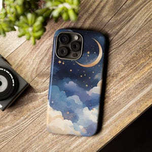 May include: A smartphone case featuring a watercolor night sky design. The case has a dark blue background with white and blue clouds, gold stars, and a gold crescent moon. The case has a glossy finish and a camera cutout.
