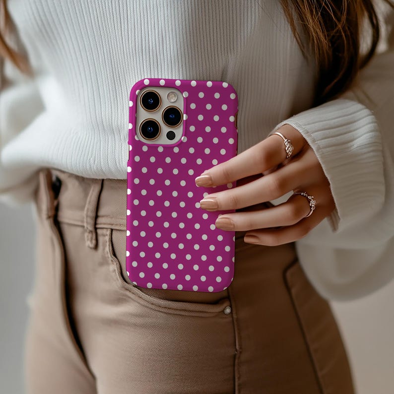 May include: A magenta phone case with a white polka dot pattern. The case is held in a pocket, showcasing the design. The phone case is a stylish accessory.