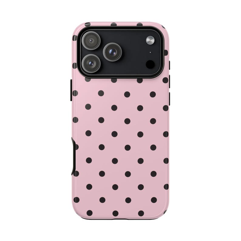 May include: A pink phone case with a black polka dot pattern. The case has a camera cutout for a triple-lens camera system. The case is designed to fit a smartphone.
