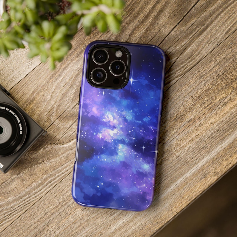 May include: A purple and blue galaxy phone case with a watercolor effect and white stars. The case has a raised camera bump with three lenses.