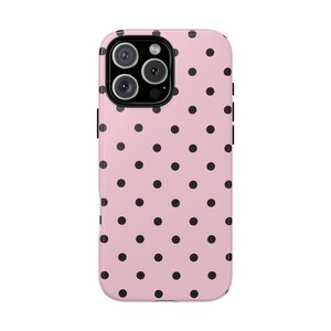 May include: A pink phone case with a black polka dot pattern. The case has a glossy finish and a camera cutout at the top. The case is designed to fit a smartphone.