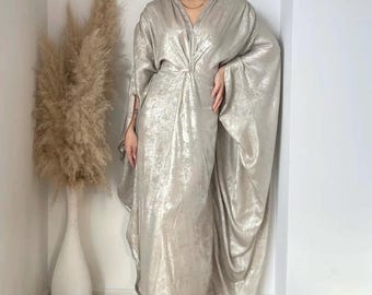 May include: A long, flowing silver dress with a V-neckline and a gathered detail at the waist. The dress has wide, flowing sleeves and a relaxed fit.