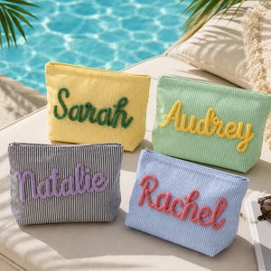 May include: Four rectangular zipped pouches made of striped fabric. The yellow pouch features the name Sarah in green, the light green pouch has Audrey in yellow, the black and white pouch has Natalie in purple, and the blue pouch has Rachel in pink.