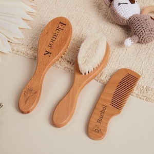 Op de afbeelding: Een baby haarverzorgingsset van licht hout. De set bevat een borstel met zachte borstelharen, een borstel met een houten handvat en een kam. De borstelhandvatten zijn gegraveerd met namen en bloemmotieven.