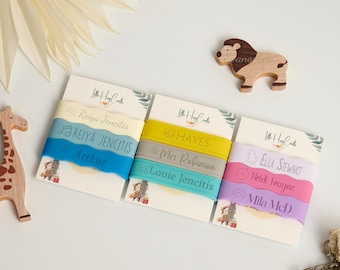 May include: A selection of personalised silicone bracelets in different colours, each with a name printed on it. The bracelets are displayed on cards with the "Little Hug Crafts" logo. A wooden lion and giraffe are also in the image.