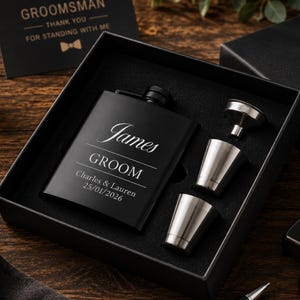 May include: A matte black metal flask engraved with the name James, the title GROOM, and the text Charles & Lauren 25/01/2026, presented in a black gift box with two silver-toned metal shot glasses and a small silver-toned metal funnel.