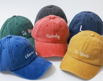 May include: A collection of six baseball caps in various colors, including blue, red, and yellow. Each cap features embroidered text, such as names and phrases. The caps have a vintage, worn look.