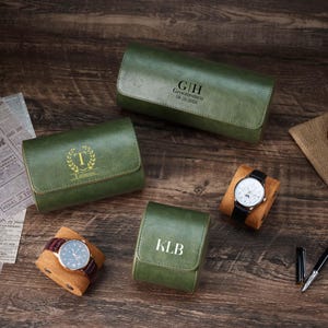 Può includere: Custodie per orologi in pelle verde con iniziali e date personalizzate. Una custodia ha inciso "G|H Groomsmen 08-26-2026". Due orologi sono esposti su cuscini marroni. Su una superficie di legno.