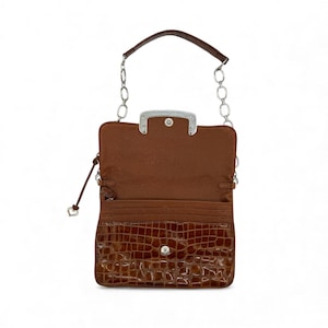 Puede incluir: Cartera de cuero marr&oacute;n abierta con una correa de cadena plateada. La parte delantera presenta un dise&ntilde;o con textura de cocodrilo. El interior es de color marr&oacute;n claro, con ranuras para tarjetas. Un cierre plateado asegura la cartera.