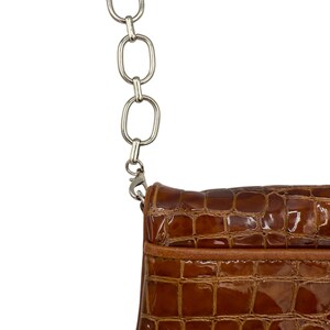 Puede incluir: Primer plano de un bolso marr&oacute;n texturizado con una correa de cadena plateada. El bolso tiene un patr&oacute;n similar al de un cocodrilo y un acabado brillante. La cadena est&aacute; hecha de eslabones grandes y ovalados.