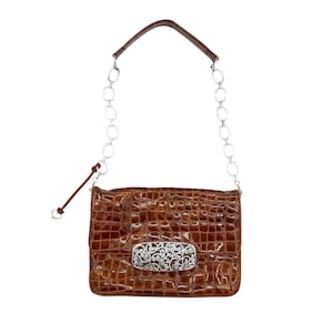 Puede incluir: Bolso de mano marr&oacute;n texturizado con una correa de cadena plateada y un cierre decorativo plateado. El bolso tiene forma rectangular y un asa de cuero. El cierre presenta un dise&ntilde;o ornamental y ondulado. El bolso es de tama&ntilde;o mediano.