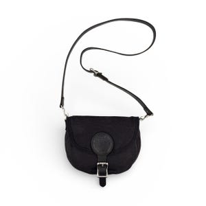 May include: Black crossbody bag with a curved shape, featuring a leather strap and buckle closure. The bag has a circular leather patch on the front and a long, adjustable strap. The bag is made of a durable material.