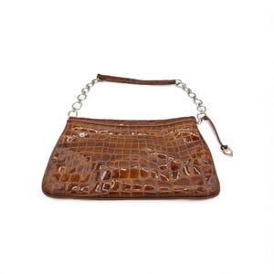 Puede incluir: Un bolso de mano rectangular marr&oacute;n con una textura brillante de piel de cocodrilo. El bolso presenta una correa de cadena plateada y un peque&ntilde;o dije en forma de coraz&oacute;n. El bolso est&aacute; dise&ntilde;ado con un asa superior y una correa de cadena.