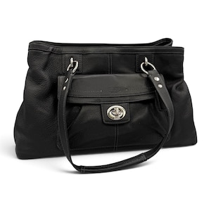 May include: A black leather handbag featuring a pebbled texture, two shoulder straps, and a front flap pocket secured with a silver-tone metal turn-lock closure. The bag includes silver hardware accents and visible stitching along the front pocket.
