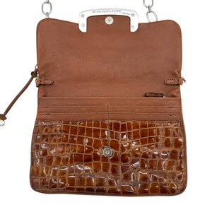 Puede incluir: Bolso bandolera de cuero marr&oacute;n abierto con solapa delantera con textura de cocodrilo. El bolso presenta una correa de cadena plateada y un cierre plateado con la inscripci&oacute;n "All you need is LOVE". El interior es de color marr&oacute;n claro.