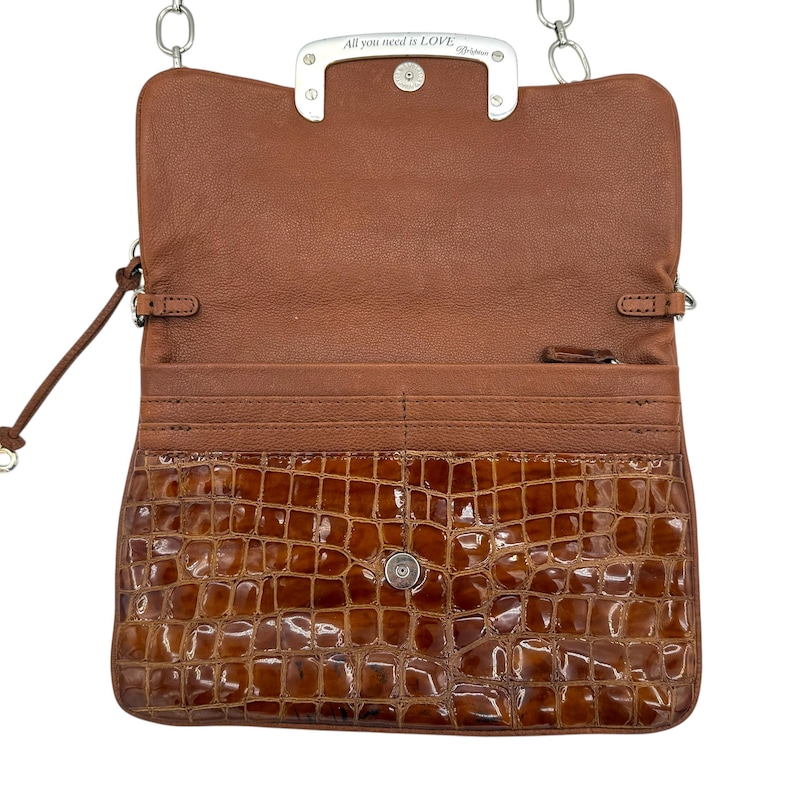 Puede incluir: Bolso bandolera de cuero marr&oacute;n abierto con solapa delantera con textura de cocodrilo. El bolso presenta una correa de cadena plateada y un cierre plateado con la inscripci&oacute;n "All you need is LOVE". El interior es de color marr&oacute;n claro.