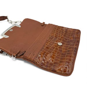 Puede incluir: Una cartera de cuero marr&oacute;n con solapa con textura de cocodrilo. La cartera tiene una correa de cadena plateada y un cierre a presi&oacute;n magn&eacute;tico. El interior es de cuero marr&oacute;n claro.