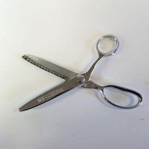 May include: A pair of silver-colored Wiss shears with a serrated blade. The shears have a loop handle and a pointed tip. The text "WISS" is printed on the blade. The shears are designed for cutting fabric.
