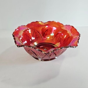 Könnte beinhalten: Eine leuchtende, irisierende rote Glasschale mit gewelltem Rand. Die Schale hat ein detailliertes Muster auf der Außenseite und eine glatte Innenseite. Der Rand ist gewellt und die Schale steht auf einem kleinen Sockel. Wahrscheinlich Vintage oder Antik.