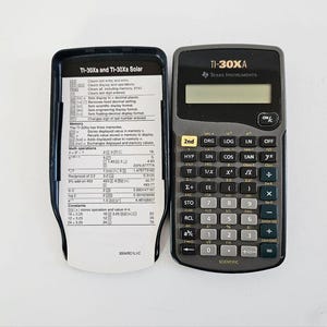 May include: A black and gray Texas Instruments TI-30XA scientific calculator with an open instruction booklet. The calculator has various buttons for mathematical functions and a display screen. The booklet provides instructions for the calculator's use.