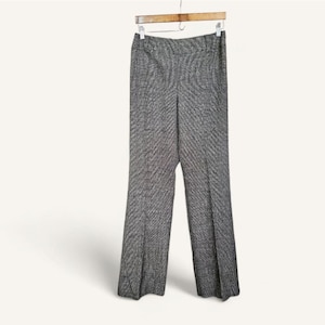 May include: Gray and white herringbone pattern trousers hanging on a wooden hanger. The pants have a straight leg design and a classic, tailored look. The fabric appears to be a medium-weight material.