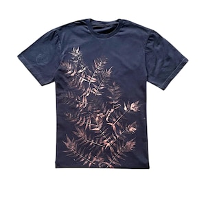 Puede incluir: Camiseta azul marino con un diseño botánico de hojas de helecho marrón claro. Las hojas están dispuestas en un patrón en capas en la parte delantera. La camiseta tiene mangas cortas y cuello redondo.