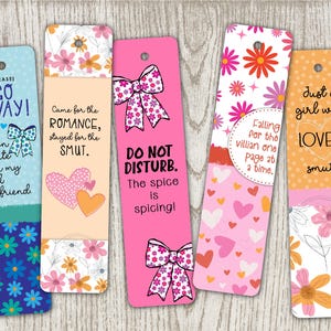 Pode incluir: Uma coleção de cinco marcadores coloridos com vários designs e texto. Os marcadores apresentam padrões florais, corações e laços. O texto inclui frases como "Go Away!", "Came for the Romance" e "Do Not Disturb."