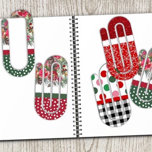 May include: A collection of decorative paper clips in various festive designs. The clips feature patterns like red glitter, polka dots, floral prints, and a black and white checkered pattern. They are arranged on a white notebook page.