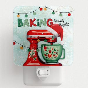 May include: A decorative night light featuring a red stand mixer with a Santa hat, and a green mixing bowl. The words "BAKING Spirits Bright" are displayed above the mixer, with festive string lights.
