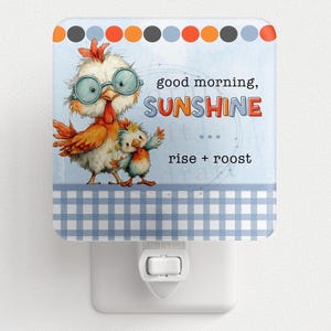 May include: A square night light with a cartoon chicken design. The light has a blue and white gingham border and a light blue background with the words "good morning, SUNSHINE" and "rise + roost". The top border has orange, gray, and blue circles.