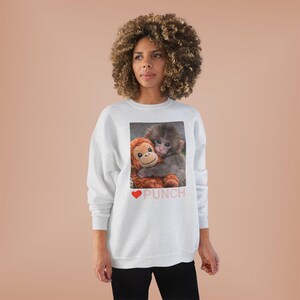 May include: A white sweatshirt featuring a graphic of two monkeys hugging. The word "PUNCH" is printed in pink below the image, with a red heart symbol. The sweatshirt is worn by a person with curly hair.