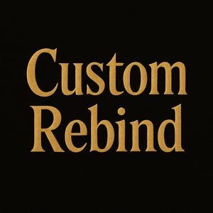 May include: Gold-colored text on a black background reads "Custom Rebind". The text has a textured appearance, suggesting a possible embossed or embroidered effect. The image is simple and direct, with a focus on the words.