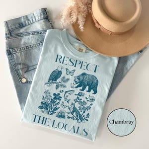 National park inspired graphic T-shirt with vintage blue wildlife illustrations including a bear, fox, eagle, fish, butterflies, and wildflowers on a Chambray Comfort Colors shirt.