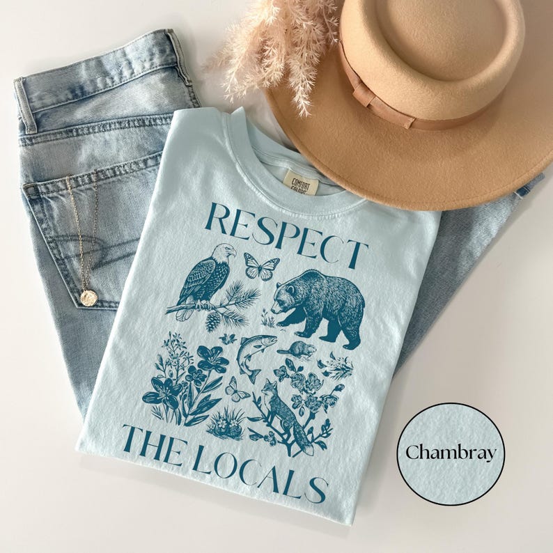National park inspired graphic T-shirt with vintage blue wildlife illustrations including a bear, fox, eagle, fish, butterflies, and wildflowers on a Chambray Comfort Colors shirt.