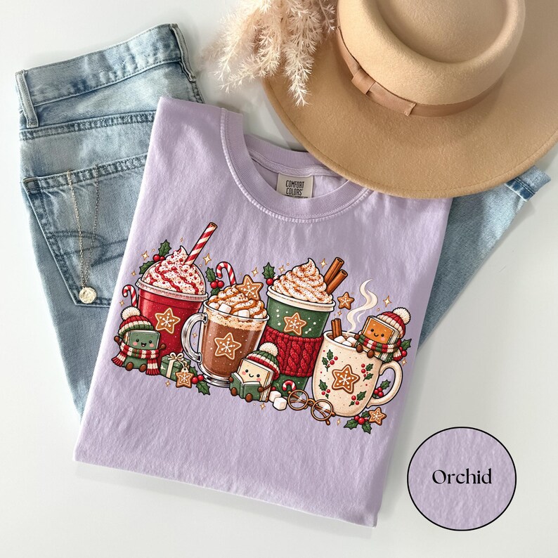 Folded Orchid lavender Comfort Colors shirt with a festive winter reading design featuring hot cocoa mugs, whipped cream, candy canes, gingerbread cookies and smiling book characters dressed in cozy scarves and knitted hats.