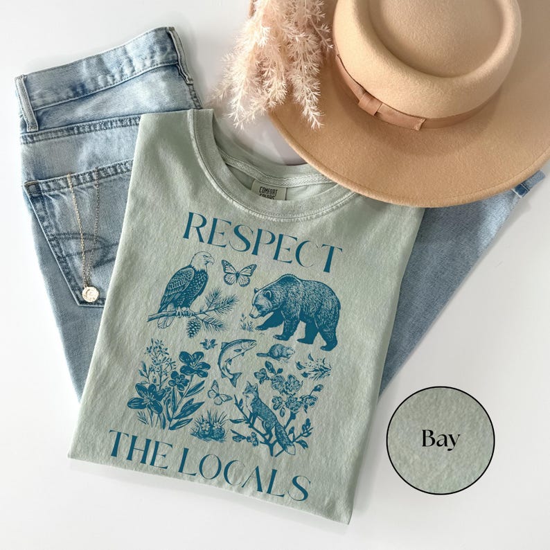 Vintage-inspired Bay Comfort Colors tee with blue “Respect The Locals” text and North American wildlife artwork including a bear, eagle, fox, fish, butterflies, and botanical illustrations.