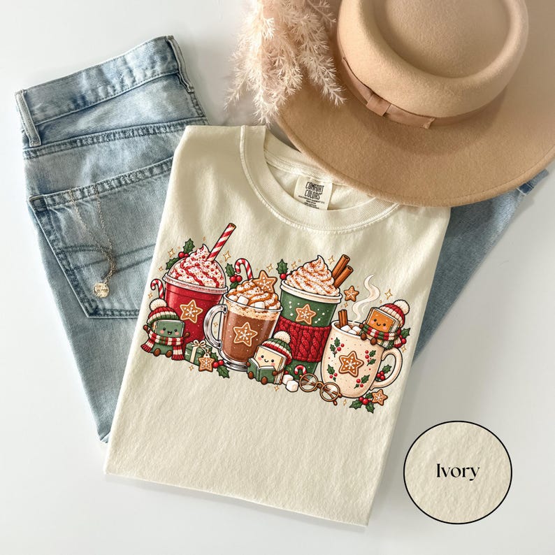44.png — Denim: Folded Denim navy Comfort Colors shirt featuring a bright Christmas reading illustration with red, green and cream hot cocoa mugs, whipped cream, candy canes, gingerbread cookies and adorable book characters wearing winter hats and scarves.