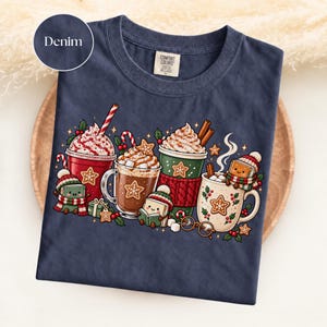 Folded Denim navy Comfort Colors shirt featuring a bright Christmas reading illustration with red, green and cream hot cocoa mugs, whipped cream, candy canes, gingerbread cookies and adorable book characters wearing winter hats and scarves.
