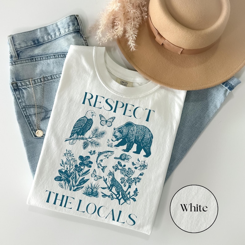 Nature lover graphic shirt featuring woodland wildlife and wildflowers in a detailed blue illustration beneath the phrase “Respect The Locals” on a White Comfort Colors T-shirt.