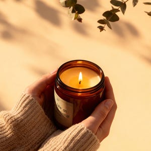 The lit amber jar candle glowing warmly in a cozy home setting, with soft shadows and eucalyptus leaves in the background.