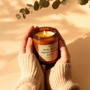 A lit soy candle in a premium amber jar being held by hands in a cozy knit sweater, creating a warm and relaxing atmosphere.