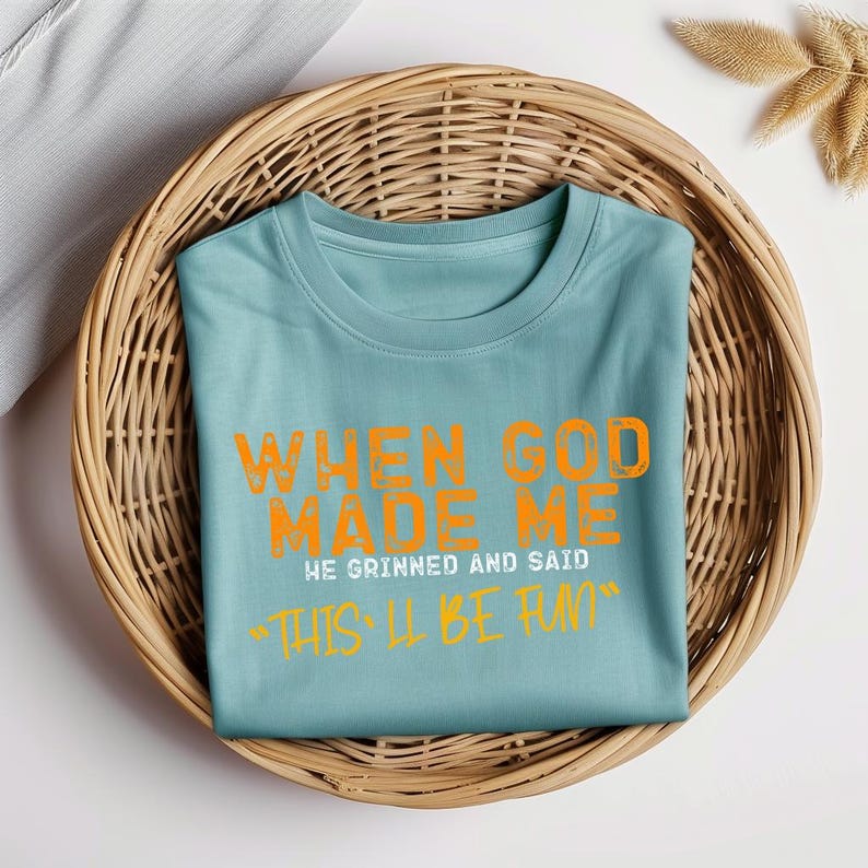 May include: A light blue t-shirt with the text "When God Made Me He Grinned And Said "This'll Be Fun"" in orange.