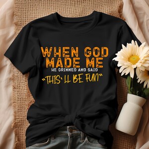 May include: Black t-shirt with orange text that reads "When God made me he grinned and said "This'll be fun""