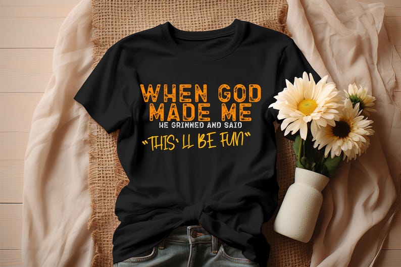 May include: Black t-shirt with orange text that reads "When God made me he grinned and said "This'll be fun""