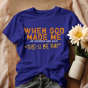 May include: A royal blue t-shirt with the text "When God Made Me He Grinned And Said "This'll Be Fun" printed in orange.