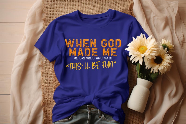 May include: A royal blue t-shirt with the text "When God Made Me He Grinned And Said "This'll Be Fun" printed in orange.